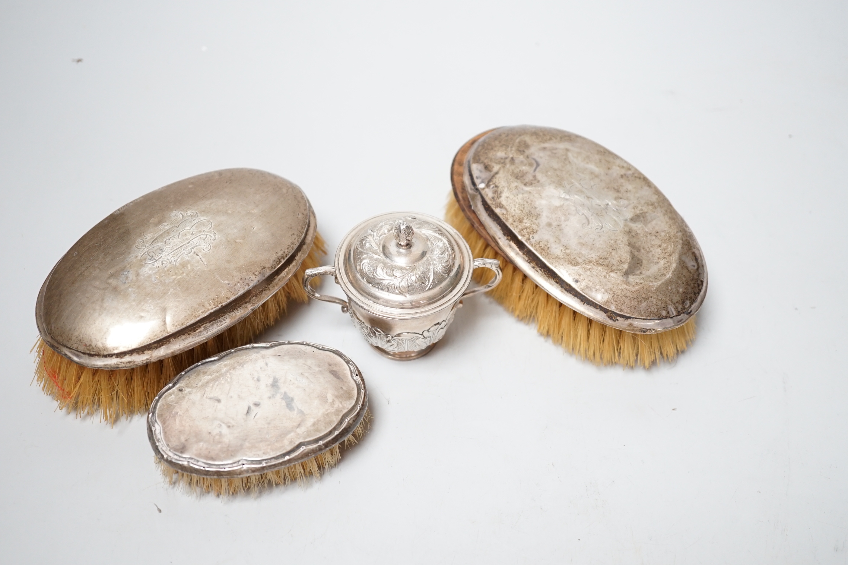 A small George V silver twin handled cup and cover, London, 1929 and three silver mounted brushes.